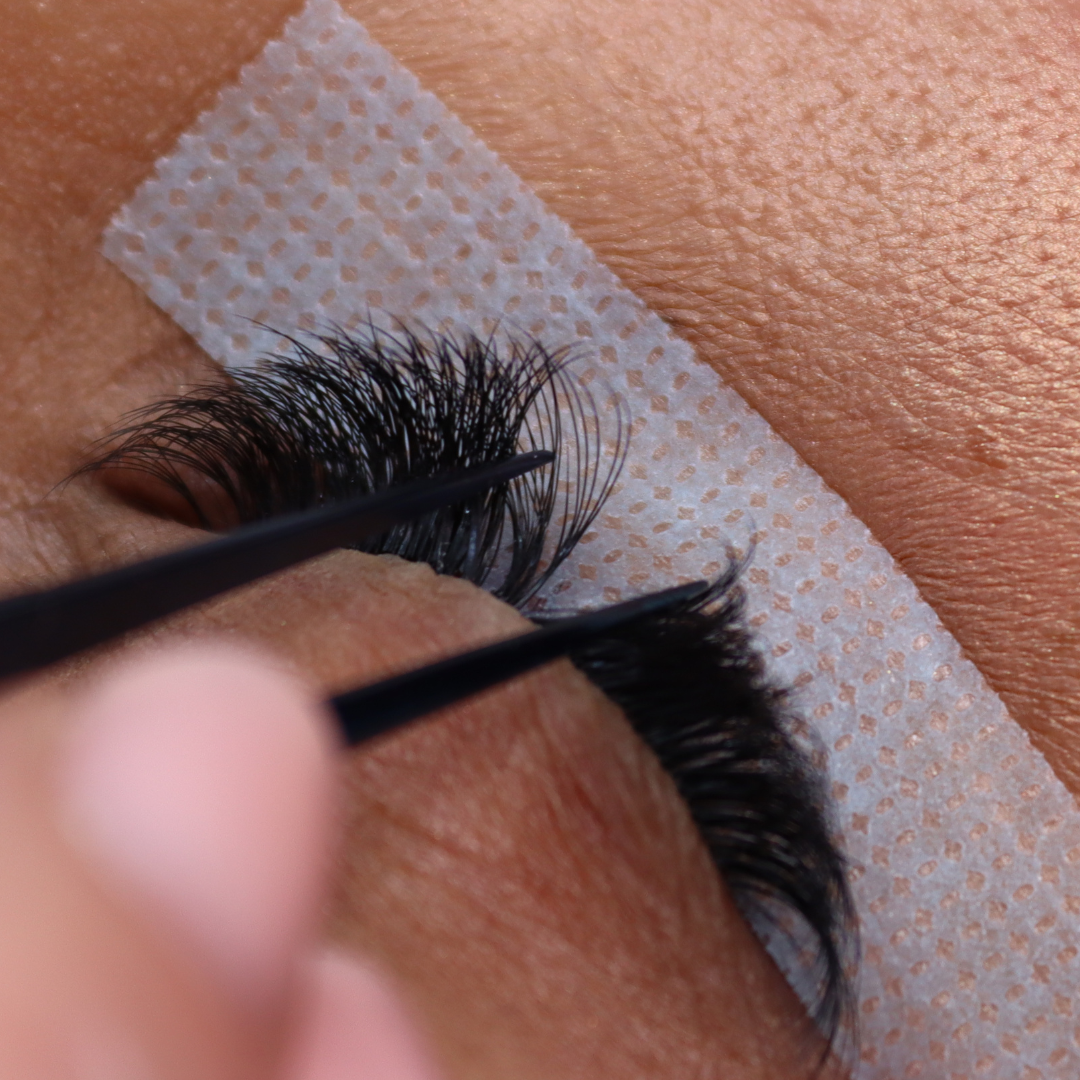 Close-up of pro-made eyelashes being applied with tweezers to a person's upper lash line.